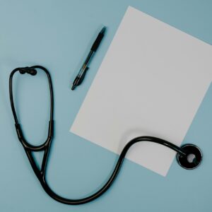 Flat lay of stethoscope, blank paper, and pen on blue surface, ideal for medical themes.